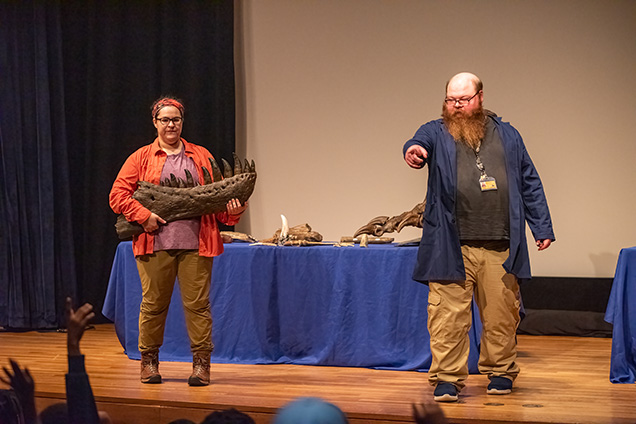 Two academy educators teaching a group of children in the audutorium about dinosaurs.
